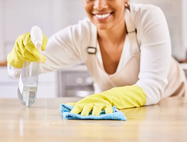 Happy unrecognizable female cleaner smiling while spraying and wiping a table surface with a cloth cleaning alone at home. One woman cleaning a counter while wearing gloves.