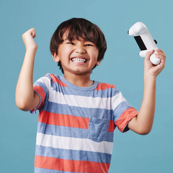 Young mixed race boy standing and holding a console controller while playing a video game against a blue background. cute child celebrating winning a game.