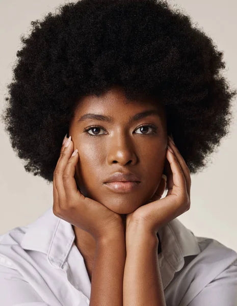 Studio portrait of a young stunning African American woman with a beautiful afro. Confident black female model showing her smooth complexion and natural beauty while posing against a grey background.