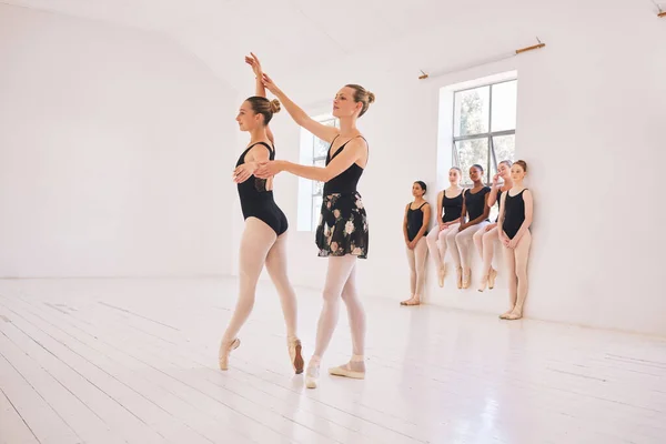 Young woman dance instructor teaching a ballet class to a group of a children in her studio. Ballerina teacher working with girl students, preparing for their recital, performance or upcoming show.