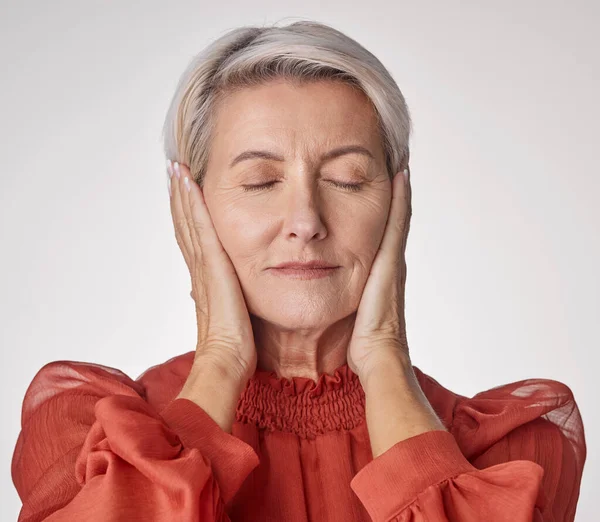 One mature woman suffering with a headache and looking stressed while posing against a grey copyspace background. Ageing woman experiencing anxiety and fear in a studio.