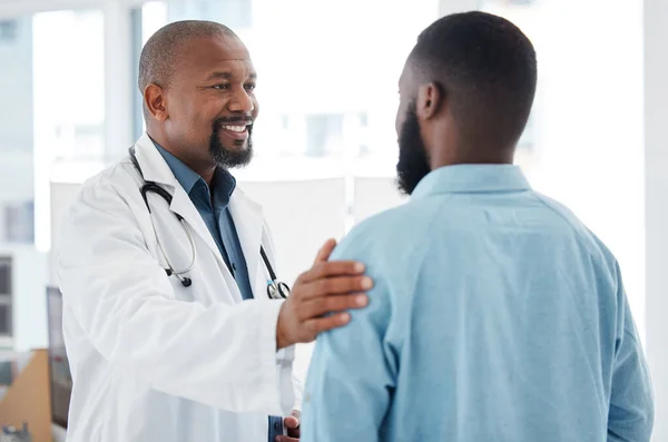 Mature doctor giving a patient support. African american doctor touching a patient on the arm. Patient in a consult with his doctor. Caring doctor giving a patient comfort and support
