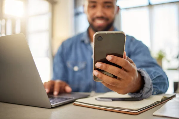 Businessman sending a text message on his smartphone at home. Young entrepreneur using his cellphone to read a message. Always online with his wireless device. Keeping connected to the internet.