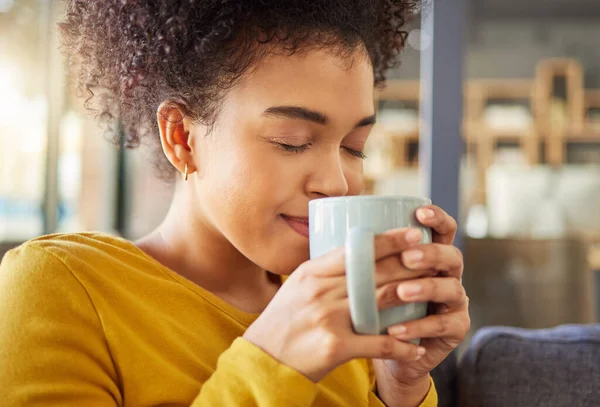 Young happy mixed race woman holding and drinking a cup of coffee at home. One cozy hispanic female smelling and enjoying a cup of tea while relaxing at home.