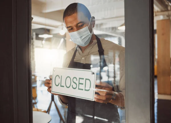 Business owner closing their shop in the pandemic. Boss hanging a closed sign in shop door in quarantine. Small business owner advertising that his restaurant is closed. Businessman wearing a mask.