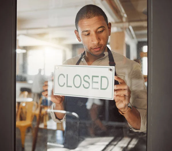 Businessman advertising that his shop is closed. Young business owner closing his restaurant. Shop owner hanging a closed sign in his store. Diner owner hanging a message in his shop entrance.