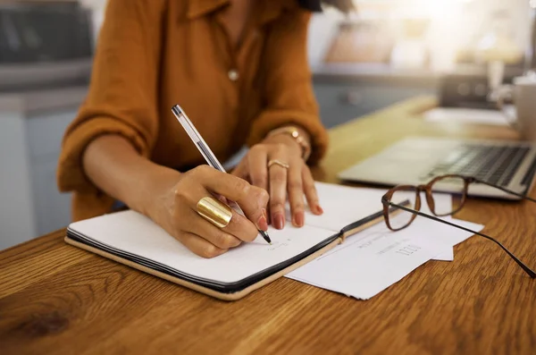 Mixed race businesswoman writing in a notebook while working from home. One hispanic female businessperson taking notes and planning in a diary.