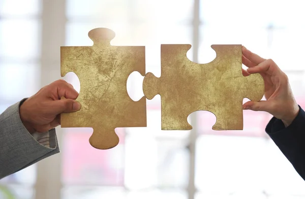Two businesspeople holding and fitting puzzle pieces together in an office at work. Business professionals solving a jigsaw problem.