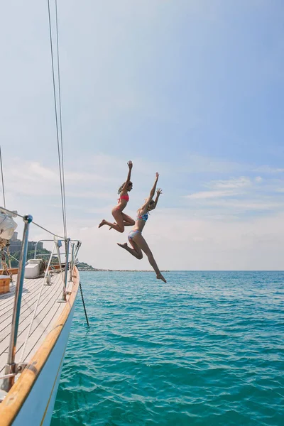 Two excited friends jumping off a boat into the ocean to swim during cruise. Two cheerful women in bikinis jumping off a boat to swim in the ocean together on holiday cruise.