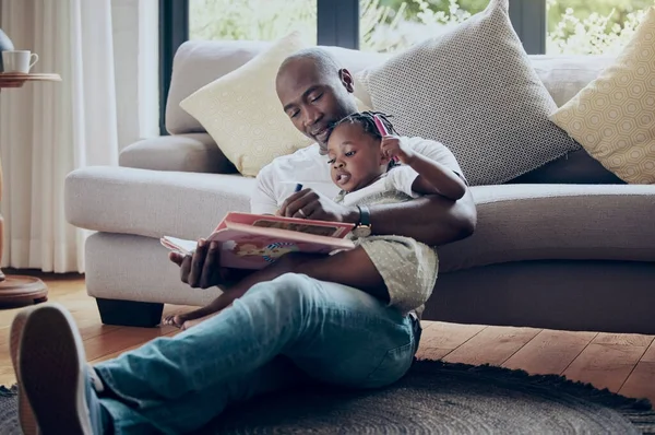 a father drawing in a book with his daughter at home.