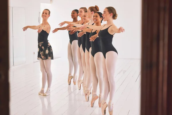 Young woman dance instructor teaching a ballet class to a group of a children in her studio. Ballerina teacher working with girl students, preparing for their recital, performance or upcoming show.