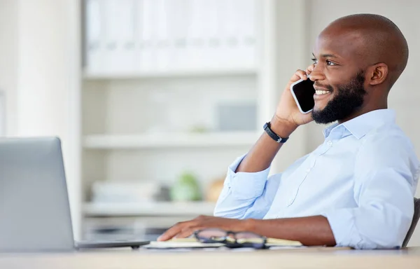 Young african american businessman on a call using a phone while working on a laptop in an office at work alone. One male business professional talking on a cellphone while working.