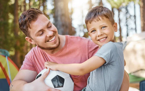 Cropped portrait of an adorable little boy and his father playing with a football while camping in the woods.