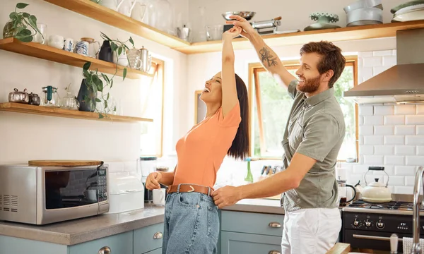 Young content interracial couple dancing in the kitchen at home. Playful caucasian boyfriend and mixed race girlfriend having fun. Husband and wife relaxing and spending time together in the morning.