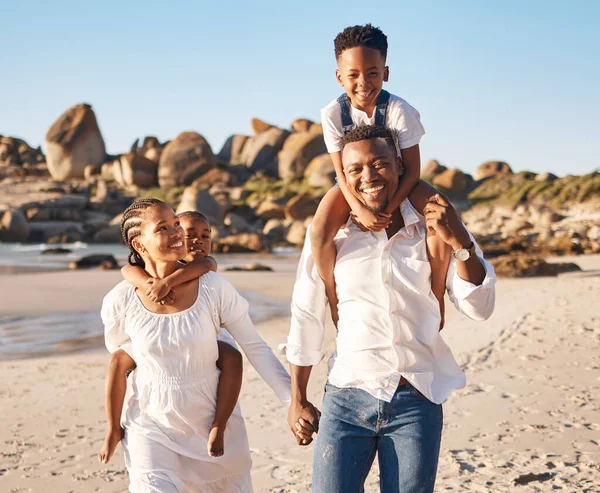 Happy young african american parents holding hands while carrying their two children and taking a walk along the beach. Young family with little daughter and son spending time together and enjoying