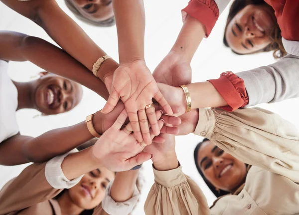 Low angle diverse group of ambitious smiling businesswomen huddled together with hands stacked in middle. Smiling ethnic team of professional colleagues feeling motivated, united, supported and ready.