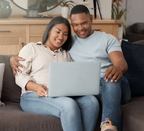 Attractive young mixed race couple relaxing on the sofa and using a laptop. Smiling African American couple watching movies while being affectionate and bonding at home together.