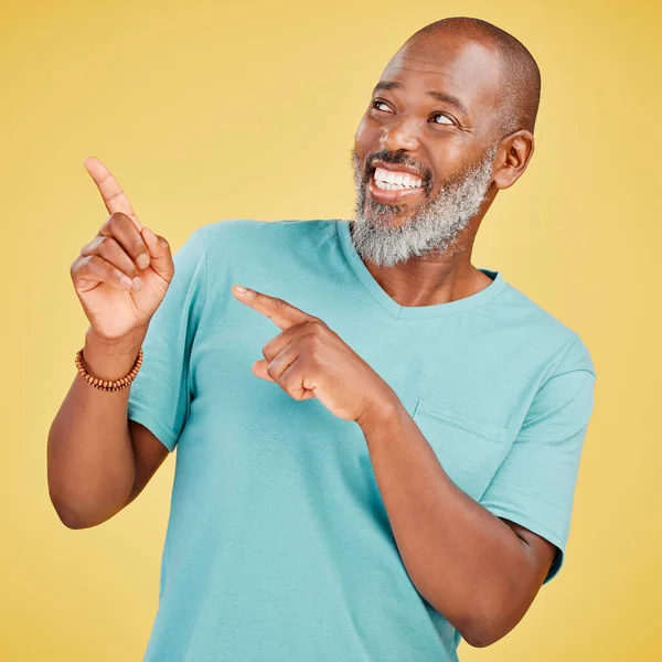 Mature african man smiling and pointing in a direction against a yellow studio background. Black guy looking happy and making a pointing gesture reacting with a smile while looking cheerful and happy