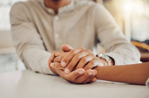 Close up of young man and woman holding hands at wooden table, from above. Loving couple expressing empathy, understanding and trust in their relationship.