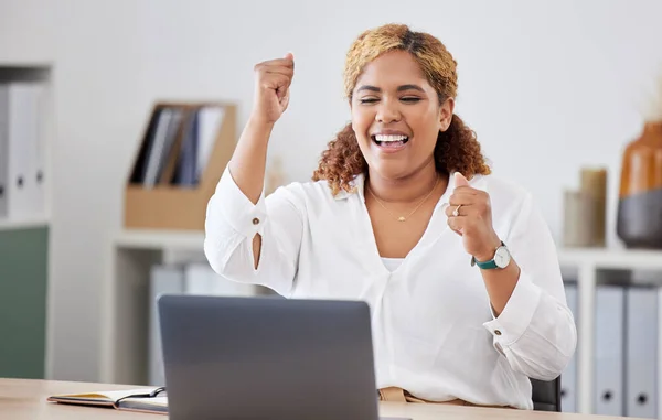 Mixed race businesswoman cheering in joy while using a laptop alone at work. One hispanic businesswoman looking excited while working on a computer at a desk in an office.