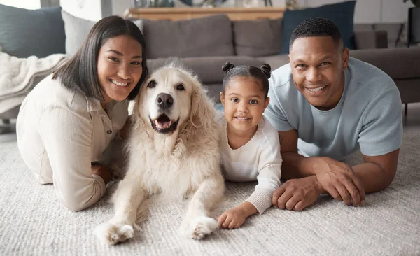 Portrait of a happy mixed race family of three relaxing on the lounge floor with their dog. Loving black family being affectionate with a foster animal. Young couple bonding with their daughter and