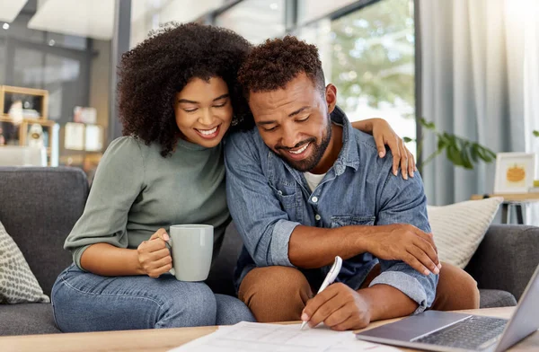 Young mixed race couple going through bills and using a laptop at a table together at home. Husband and wife planning and working on documents.
