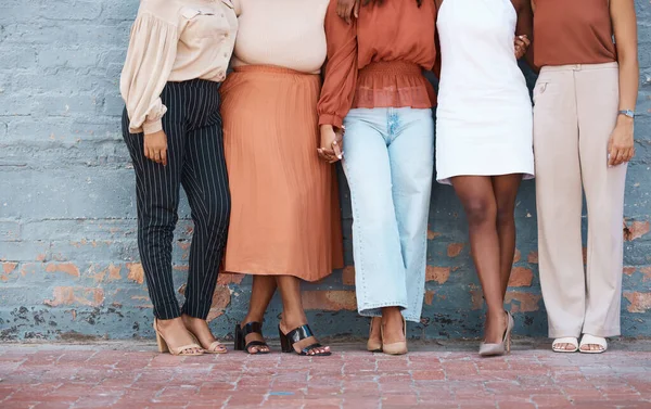 Group of five businesswomen standing against a wall in outside in the city. Legs of friends standing outdoors together from below. Caring businesspeople standing together.