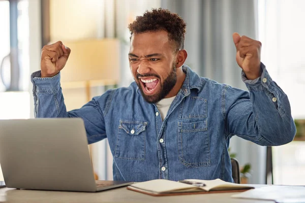 Young businessman looking at his laptop and cheering. Excited businessman working from home cheering. Cheerful entrepreneur excited about his success. Businessman working from home on his laptop.