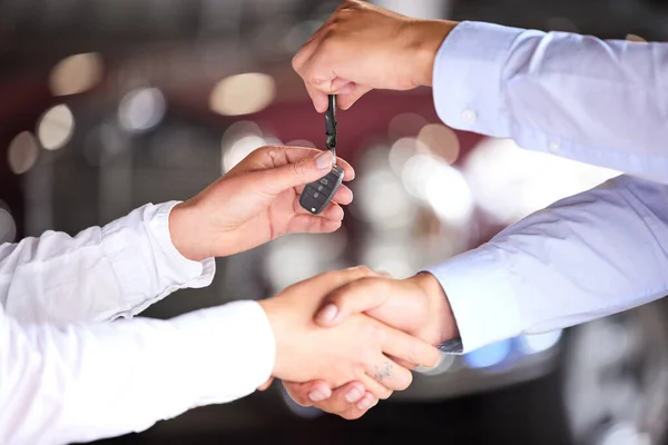 an unrecognizable car salesman shaking hands with a customer on the showroom floor of his car dealership.