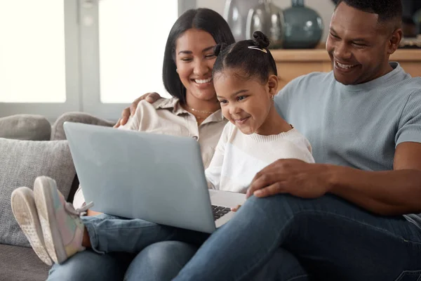 A happy mixed race family of three relaxing on the sofa at home. Loving black family being affectionate on the sofa while using a laptop and streaming. Young couple bonding with their daughter and