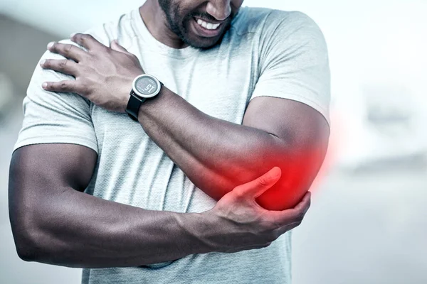 Closeup fit mixed race man holding his elbow in pain while exercising outdoors. Unrecognizable male athlete suffering with a joint injury highlighted by glowing cgi. You can get hurt during a workout.