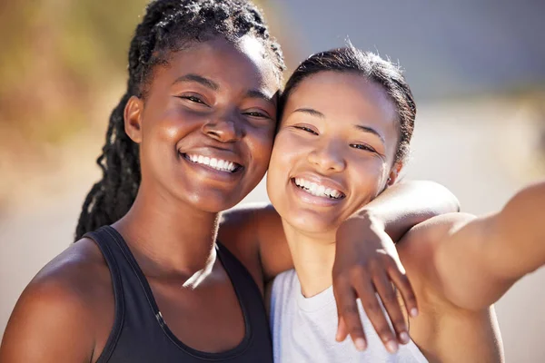 Two female athletes smiling and posing together while exercising outdoors. Two happy female friends in sportswear smiling and standing together while out for a run.