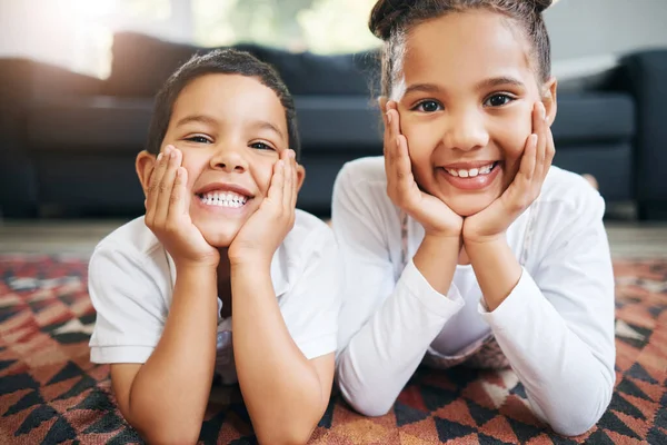 Portrait of two mixed race young siblings lying on the floor together at home and smiling. Little hispanic boy and girl having fun in the lounge at home.