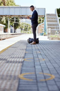 Siyah iş adamı yalnız seyahat ediyor. Tren istasyonunda tren bekleyen genç bir Afro-Amerikalı işadamı tren istasyonunda işe giderken cep telefonunu kullanıyor..