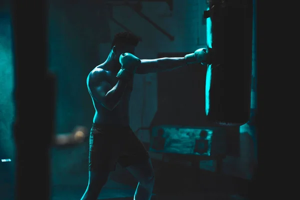 一个无法辨认的拳击手在黑暗的体育馆里与一个拳打脚踢的包斗的轮廓 男子运动员正在为即将到来的比赛做准备 年轻武术家的训练和练习 — 图库照片