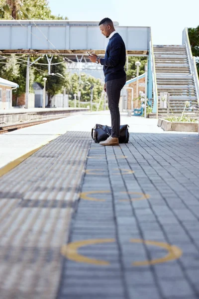 Black businessman travelling alone. A young african american businessman waiting for a train at a railway station and using his wireless cellphone during his commute at a train station.