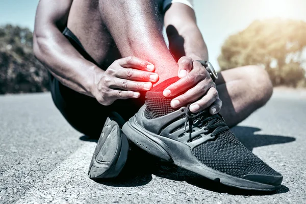 Closeup fit mixed race man holding his ankle in pain while exercising outdoors. Unrecognizable male athlete suffering with a joint injury highlighted by glowing cgi. You can get hurt during a workout.