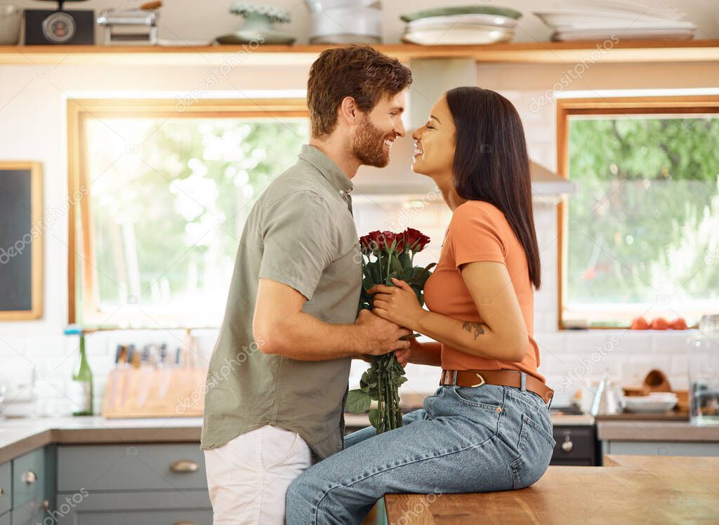 Young content caucasian boyfriend giving his cheerful mixed race girlfriend a bouquet of flowers at home. Happy hispanic wife receiving roses from her husband. Interracial couple bonding together at