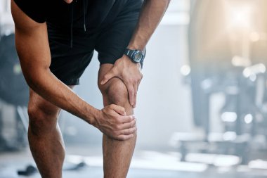 Unknown trainer alone in gym and suffering from knee injury. One coach standing and rubbing leg during workout in exercise health club. One man in fitness centre feeling pain during routine training.