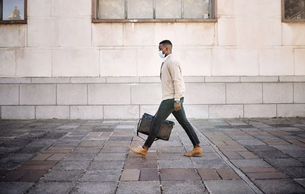 Black businessman travelling alone.A african american businessman walking around town with his luggage while wearing mask to protect himself from the corona virus in the city.