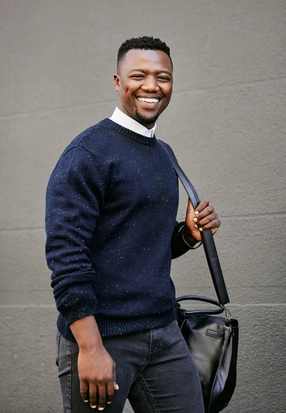 Portrait of a young businessman standing in the street in the city smiling and looking happy on a sunny day. African american male expressing happiness on his face.