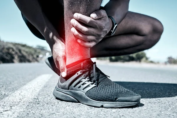 Closeup fit mixed race man holding his ankle in pain while exercising outdoors. Unrecognizable male athlete suffering with a joint injury highlighted by glowing cgi. You can get hurt during a workout.