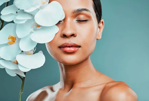 Studio portrait of an attractive young mixed race woman posing with a orchid against a green background. Latin female posing with a plant with her smooth soft skin.