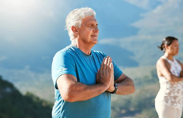 Senior man meditating with joined hands and closed eyes breathing deeply. Mature people doing yoga in nature living a healthy active lifestyle in retirement.