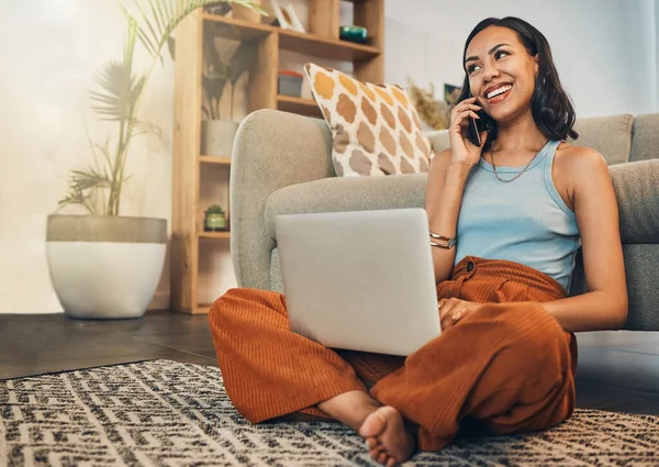 .Beautiful mixed race woman using blogging laptop and cellphone to talk to clients in home living room. Hispanic entrepreneur sitting cross legged alone on lounge floor and networking on technology.