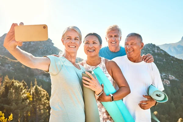 Group of active seniors posing together for a selfie or video call on a sunny day against a mountain view background. Happy diverse retirees taking photo after group yoga session. Living healthy and