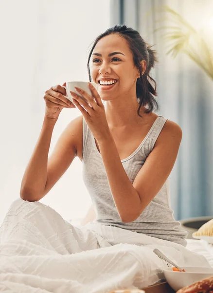 A beautiful young Hispanic woman enjoying a warm cup of coffee for breakfast. One mixed race female drinking tea while sitting in bed and laughing.