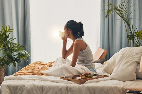 A beautiful young Hispanic woman enjoying a warm cup of coffee for breakfast. One mixed race female drinking tea while sitting in bed and daydreaming.