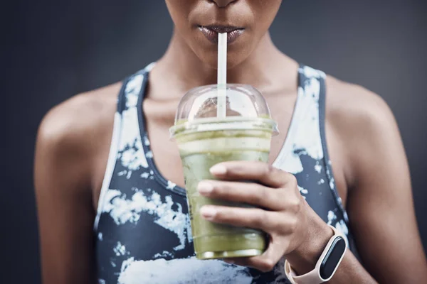 Closeup of one active woman drinking a healthy green detox smoothie while exercising outdoors. Female athlete sipping on fresh fruit juice with straw in plastic cup to cleanse and provide energy for