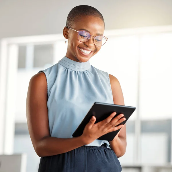 Young cheerful african american businesswoman working on a digital tablet alone at work. Happy black woman smiling while using social media on a digital tablet. Businessperson checking an email on a